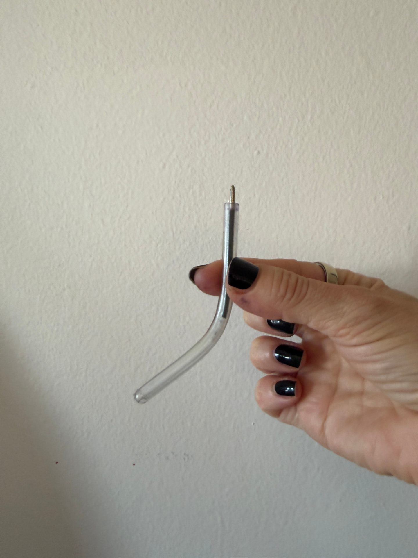 A hand holding the short, clear, flexible safety pen upright